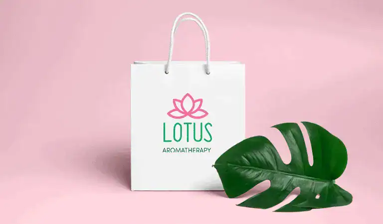 A white paper bag that says "Lotus Aromatherapy" and a big green leaf lying next to it